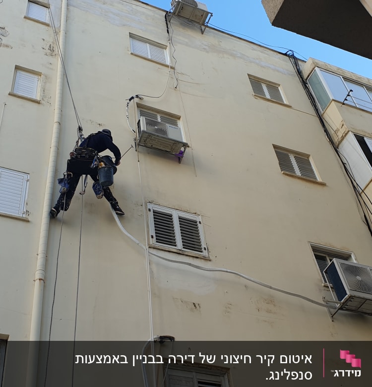 אדם על חבל מבצע איטום קיר חיצוני של בניין